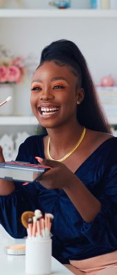 happy young african american woman streaming a beauty vlog from home, online content creator applying a makeup on