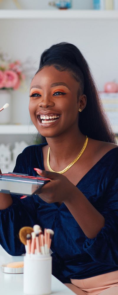 happy young african american woman streaming a beauty vlog from home, online content creator applying a makeup on